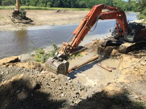 Backhoe installing wood on streambank