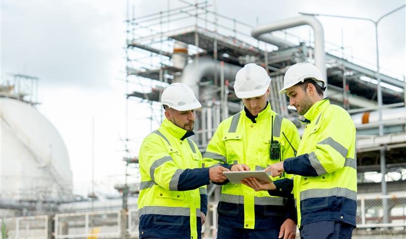 People in hard hats reviewing data on a tablet in front of a facility