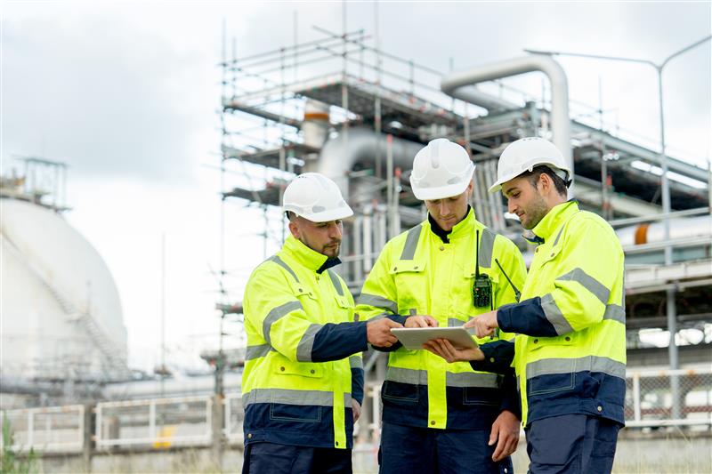 People in hard hats reviewing data on a tablet in front of a facility